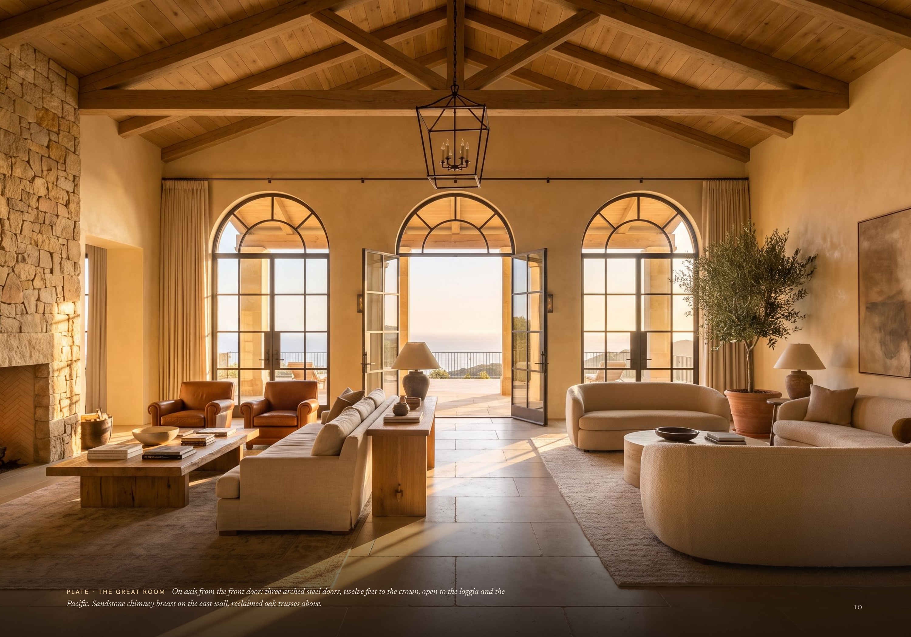 P L AT E · T H E G R E AT R O O M On axis from the front door: three arched steel doors, twelve feet to the crown, open to the loggia and the Pacific. Sandstone chimney breast on the east wall, reclaimed oak trusses above. 10